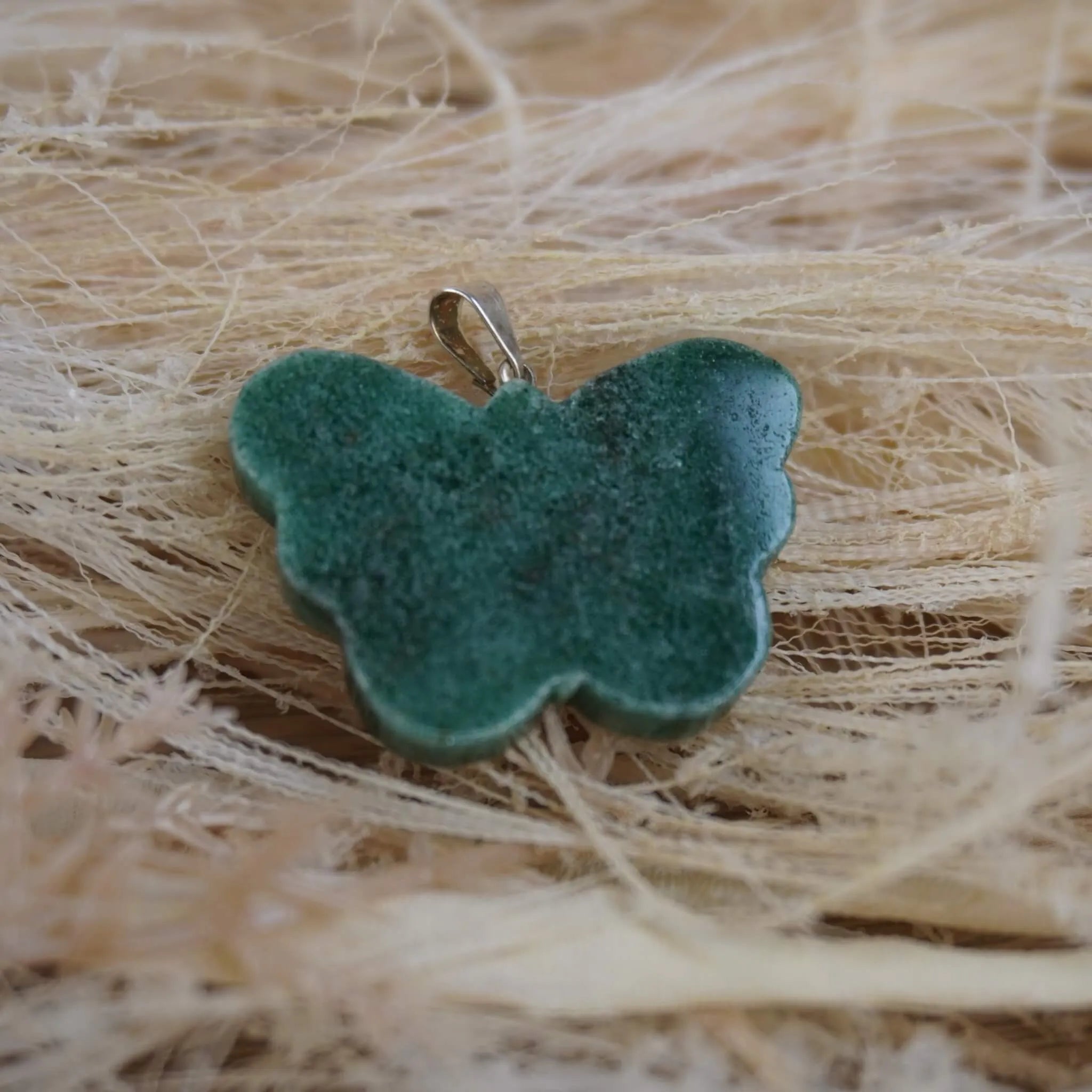 Grüner Aventurin Schmetterling Kettenanhänger auf hellen Naturfasern liegend