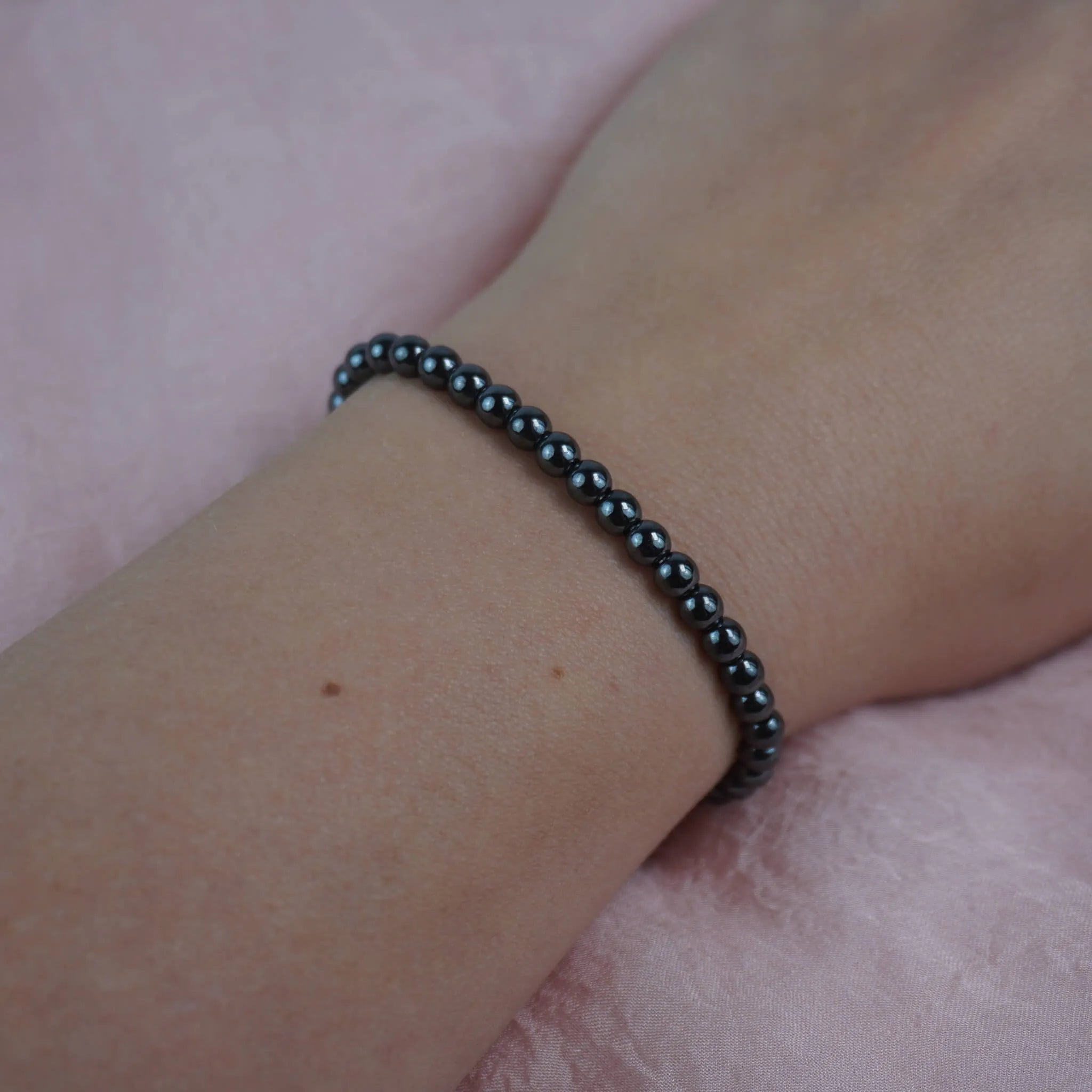 Hämatit Kugelarmband schlicht am Handgelenk vor rosa Hintergrund