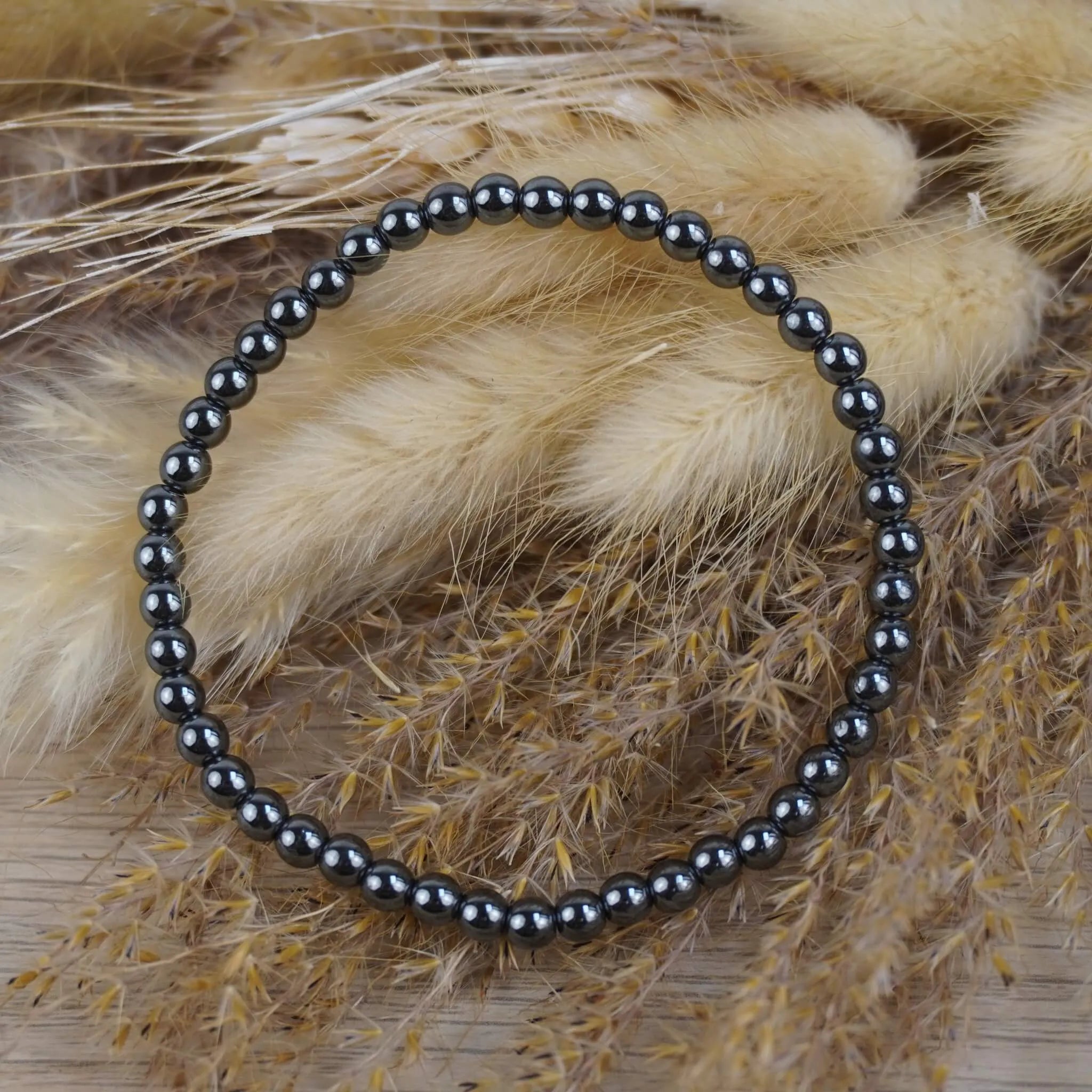 Hämatit Kugelarmband vor beigen Trockenblumen im natürlichen Boho-Stil