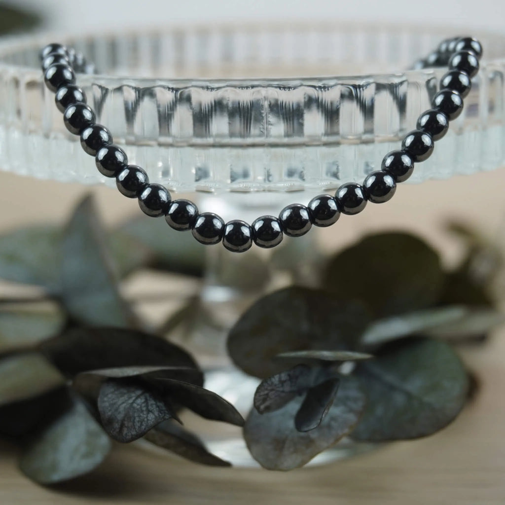 Hämatit Kugelarmband an Glas-Schale mit dunklen Eukalyptusblättern arrangiert