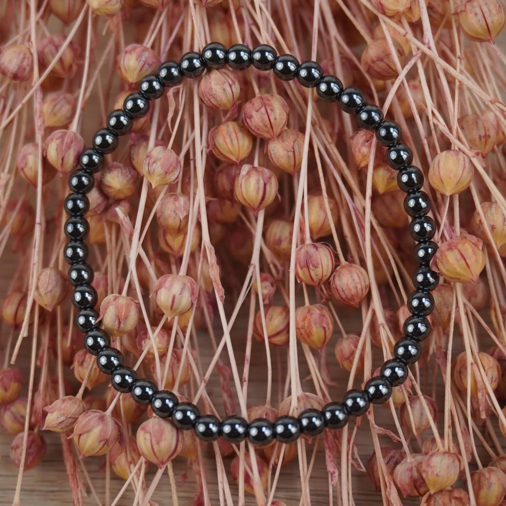 Hämatit Kugelarmband vor rosafarbenen Trockenblumen dekorativ präsentiert