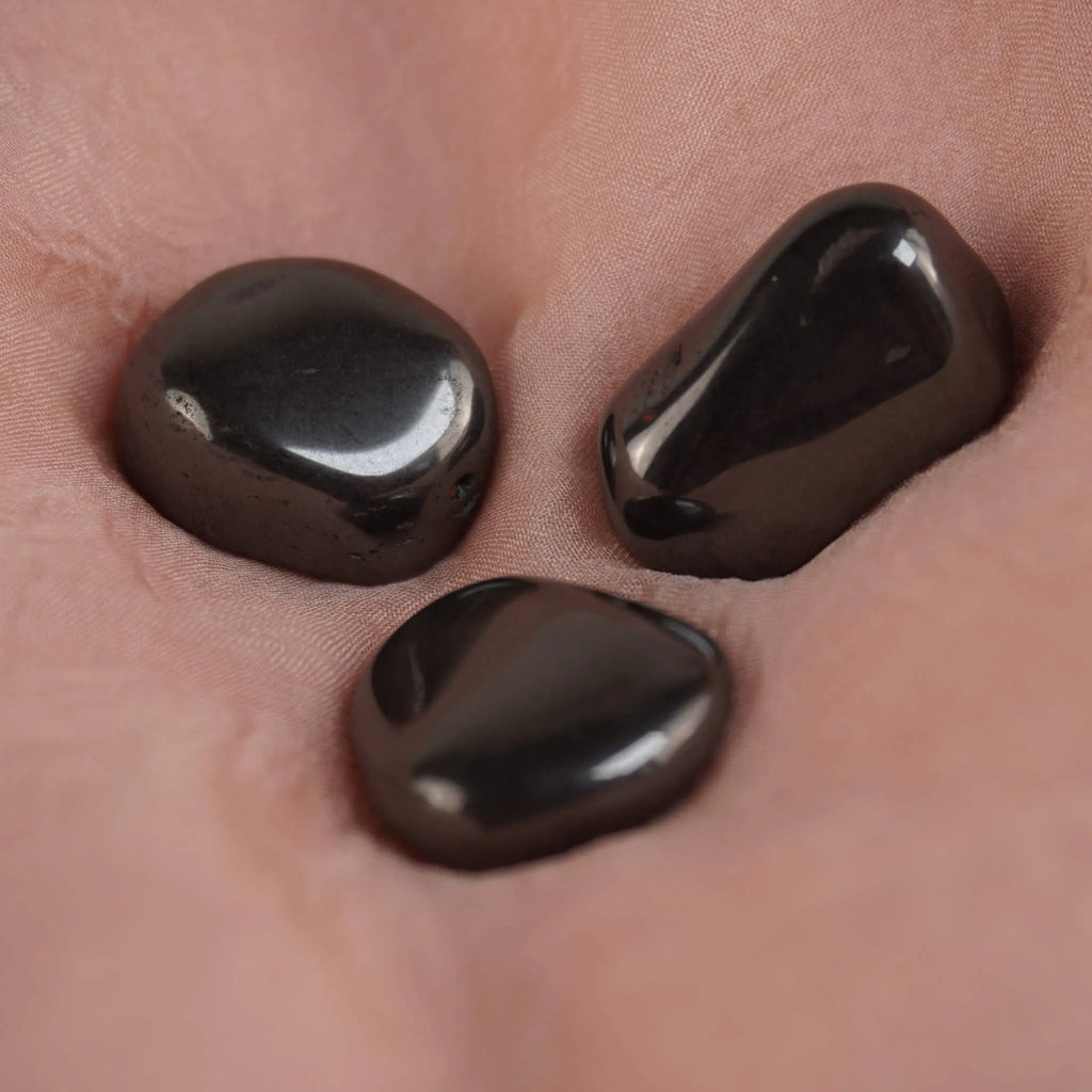 Drei Hämatit Trommelsteine arrangiert auf rosafarbenem Stoff