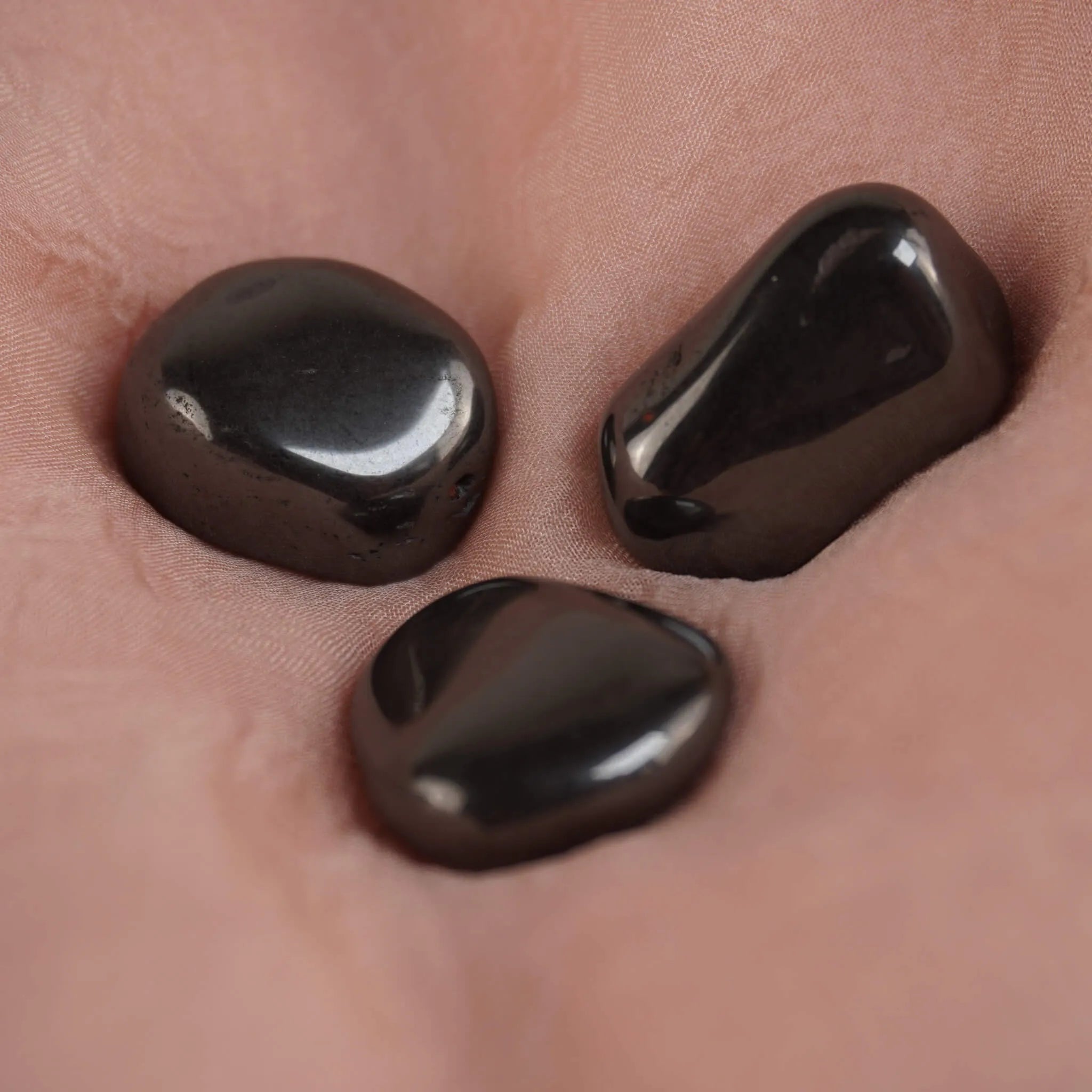 Drei Hämatit Trommelsteine arrangiert auf rosafarbenem Stoff