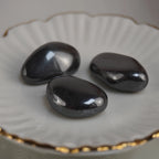 Drei polierte Hämatit Trommelsteine auf weißer Schale mit Goldrand