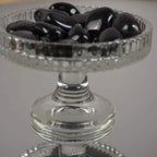 Mehrere Hämatit Trommelsteine in einem erhöhten Glaskelch präsentiert