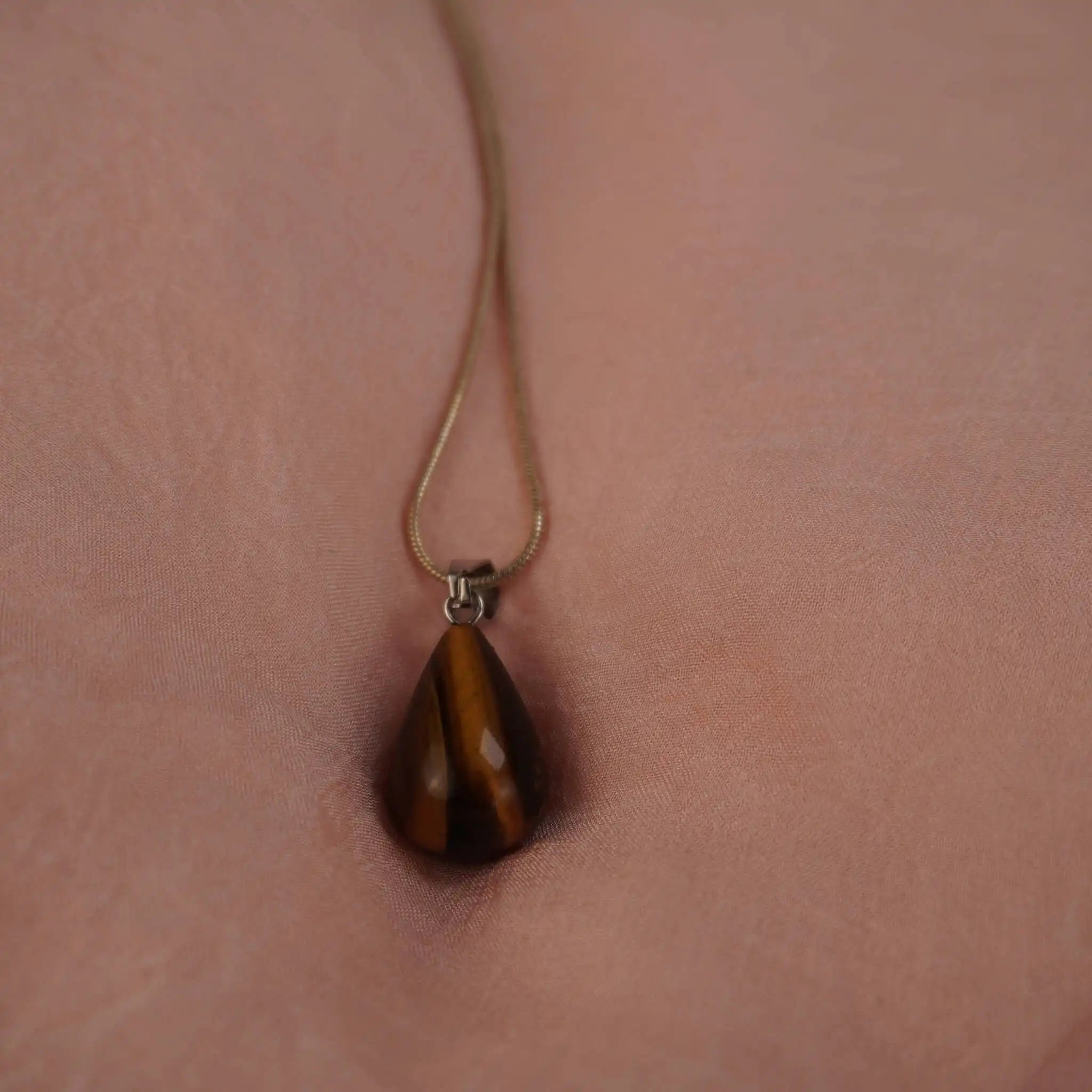 Elegante Halskette mit Tigerauge Tropfenanhänger an versilberter Kette auf rosa Hintergrund