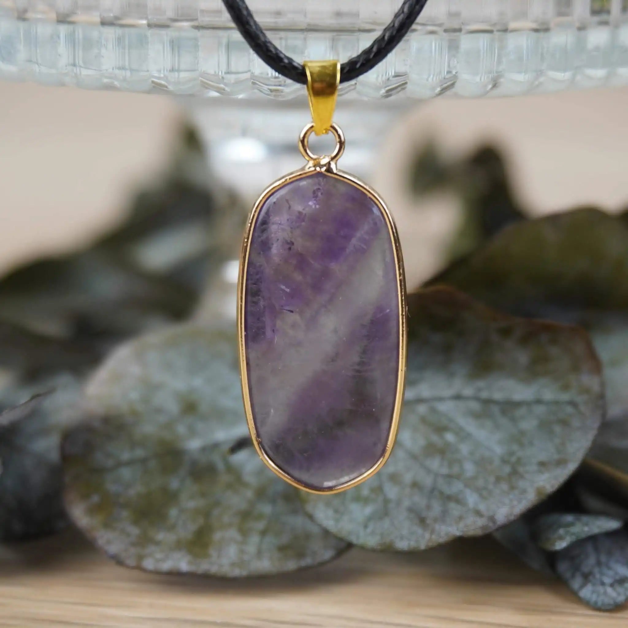 Halskette mit Amethyst Anhänger vor Glasgefäß mit Blättern