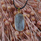 Halskette mit Labradorit Anhänger in goldfarbener Fassung auf rosa Blütenarrangement