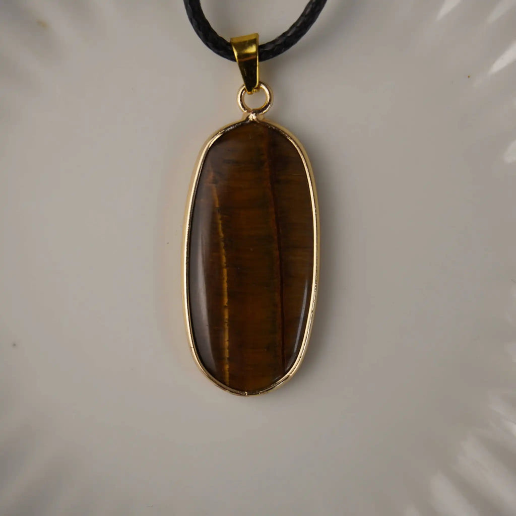 Elegante Halskette mit Tigerauge Anhänger in goldfarbener Fassung auf hellem Keramik