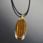 Elegante Halskette mit Tigerauge Anhänger in goldfarbener Fassung an schwarzem Band auf glänzendem Hintergrund