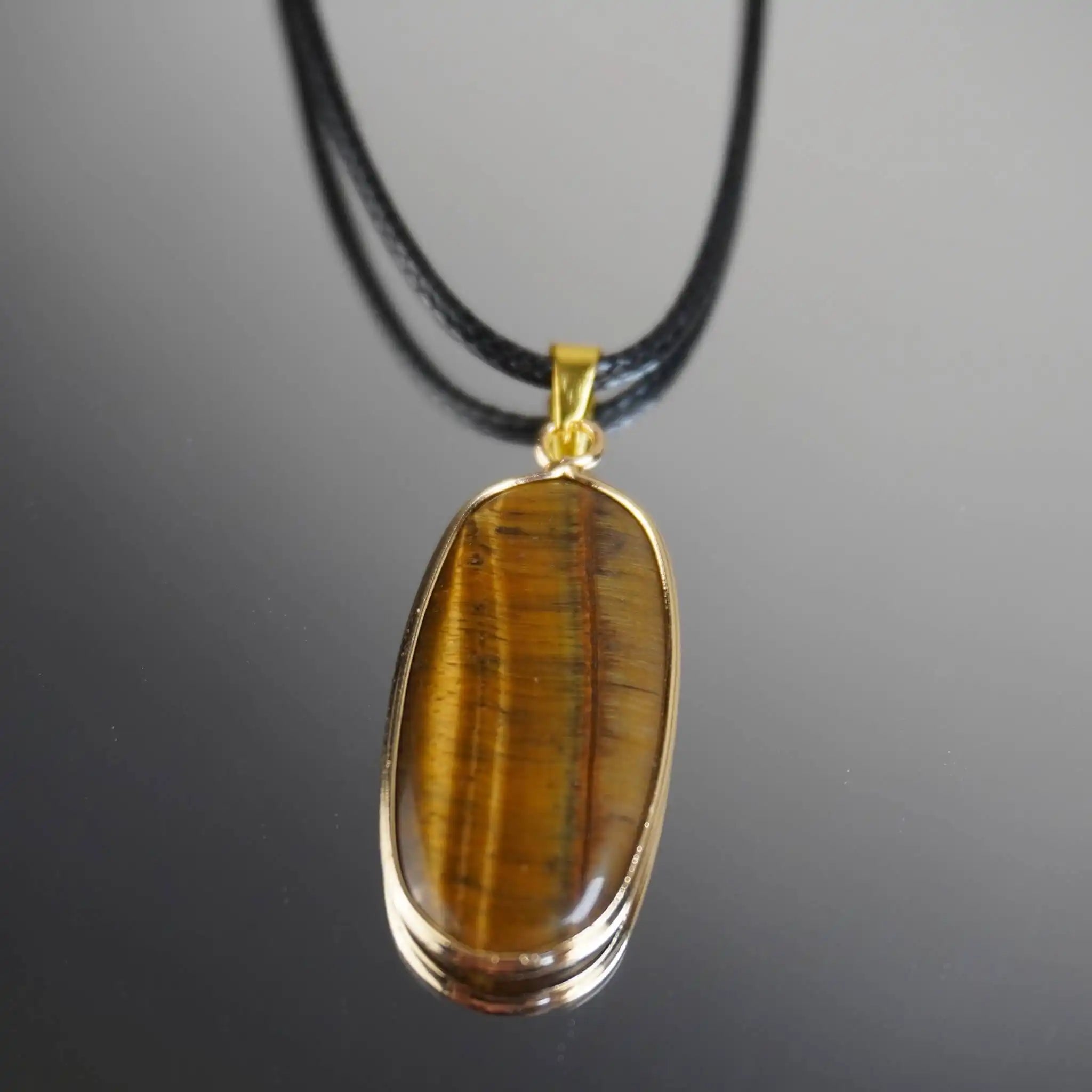 Elegante Halskette mit Tigerauge Anhänger in goldfarbener Fassung an schwarzem Band auf glänzendem Hintergrund