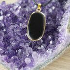Schwarzer Onyx-Anhänger in goldfarbener Fassung auf Amethyst-Kristallen
