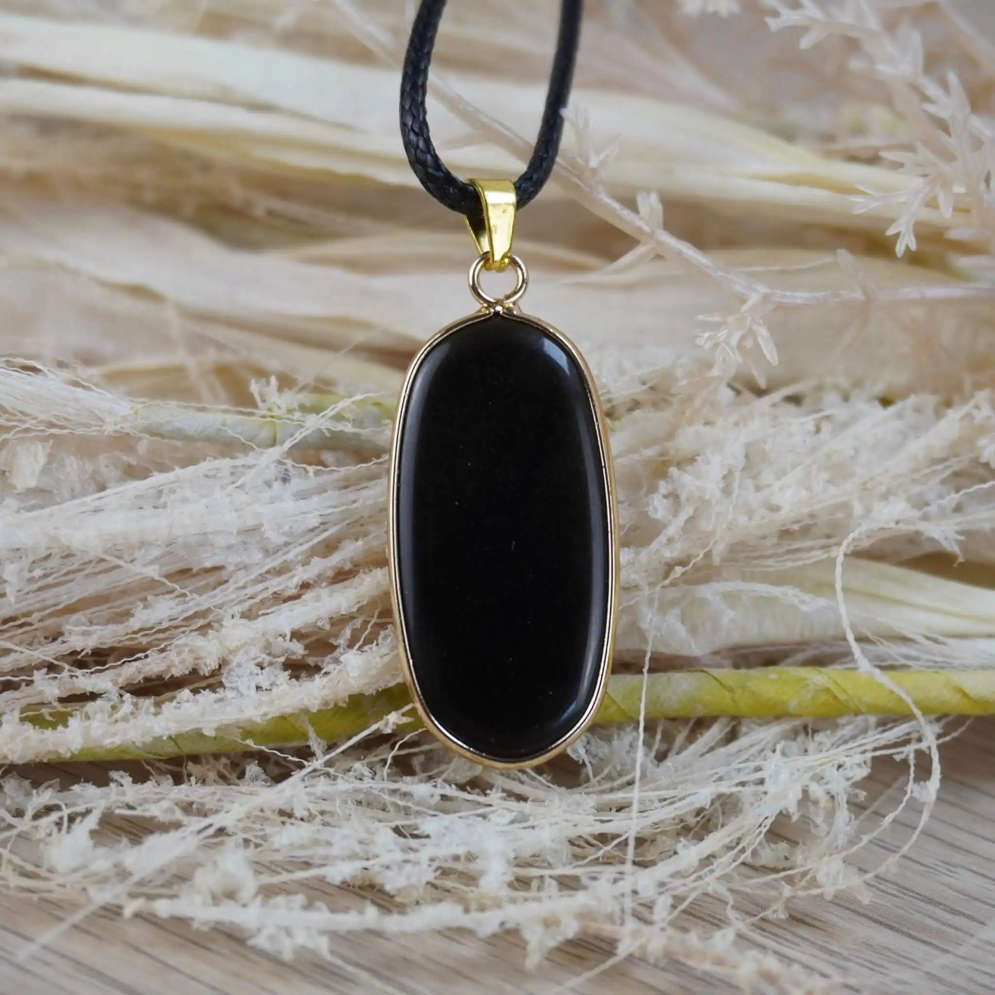 Schwarzer Onyx-Anhänger in goldfarbener Fassung dekoriert mit Naturmaterialien