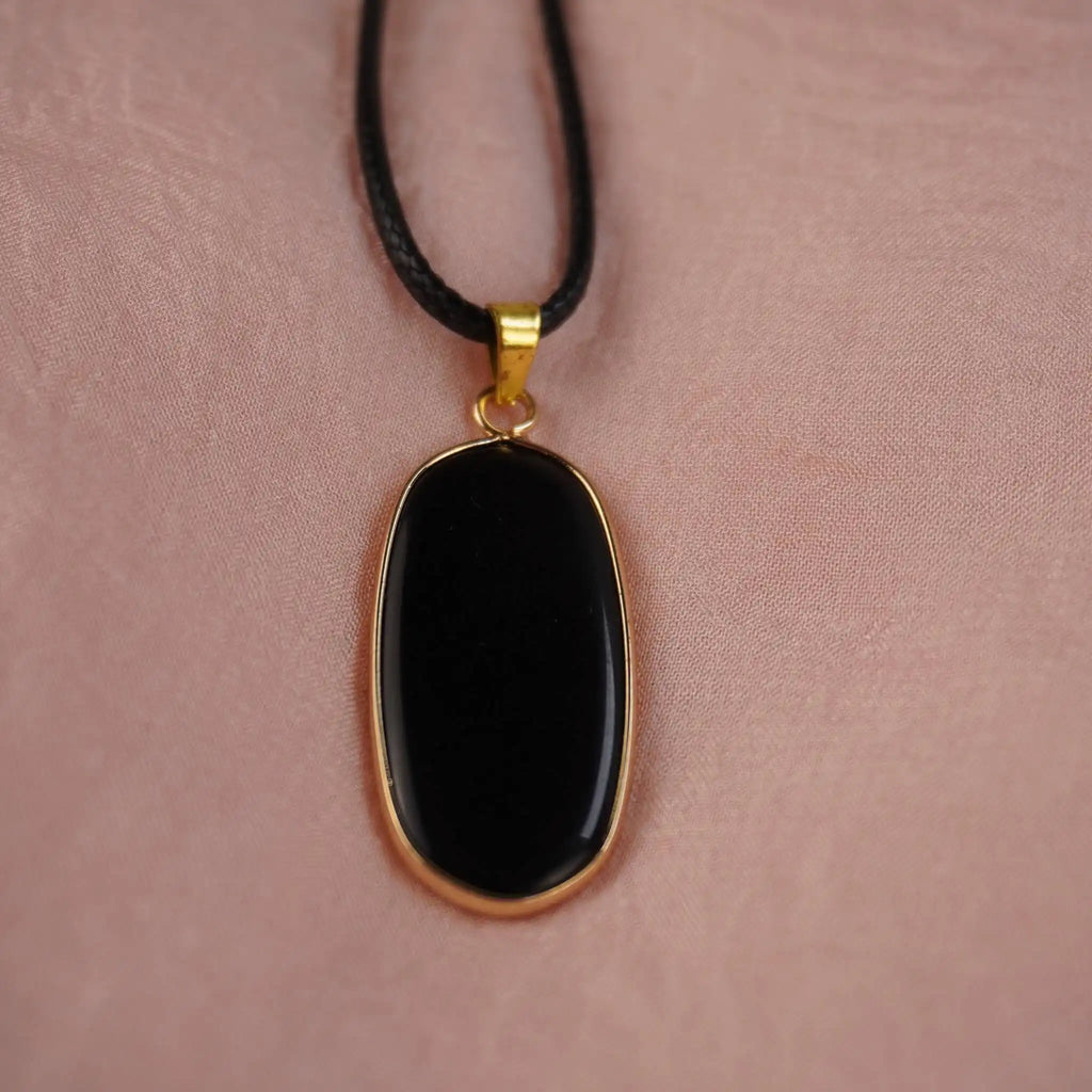 Halskette mit schwarzem Onyx-Anhänger in goldfarbener Fassung auf rosa Hintergrund