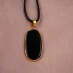 Halskette mit schwarzem Onyx-Anhänger in goldfarbener Fassung auf rosa Hintergrund