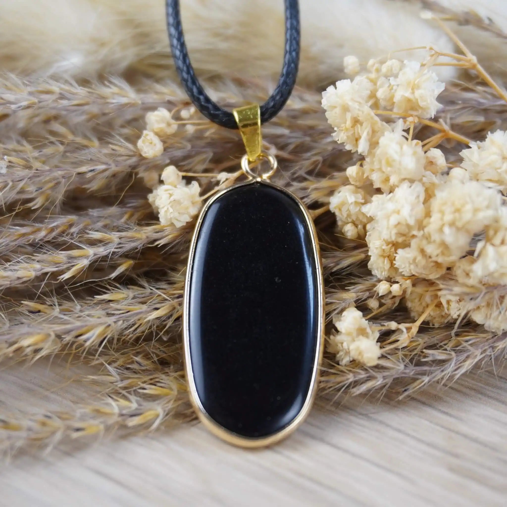 Halskette mit schwarzem Onyx-Anhänger zwischen getrockneten Blüten und Gräsern