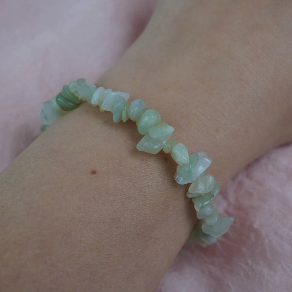 Jade Splitterarmband am Handgelenk getragen, vor weichem rosa Hintergrund