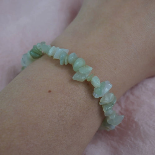 Jade Splitterarmband am Handgelenk getragen, vor weichem rosa Hintergrund