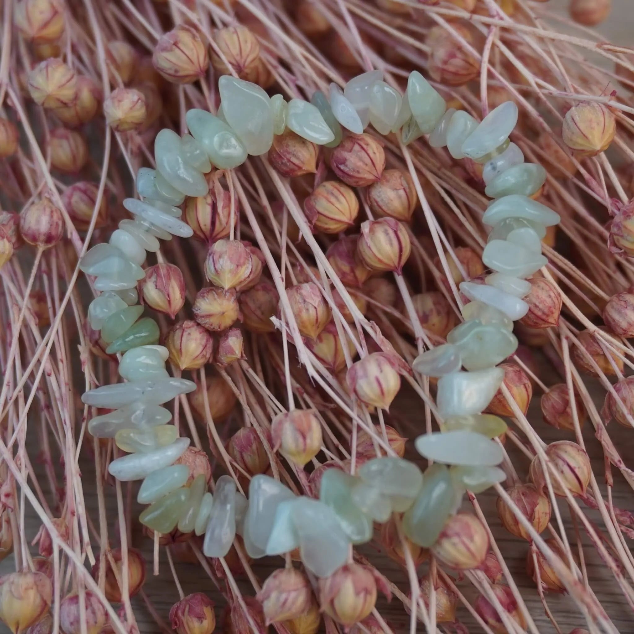 Jade Splitterarmband vor rosafarbenen Trockenblumen, sanfter Farbkontrast