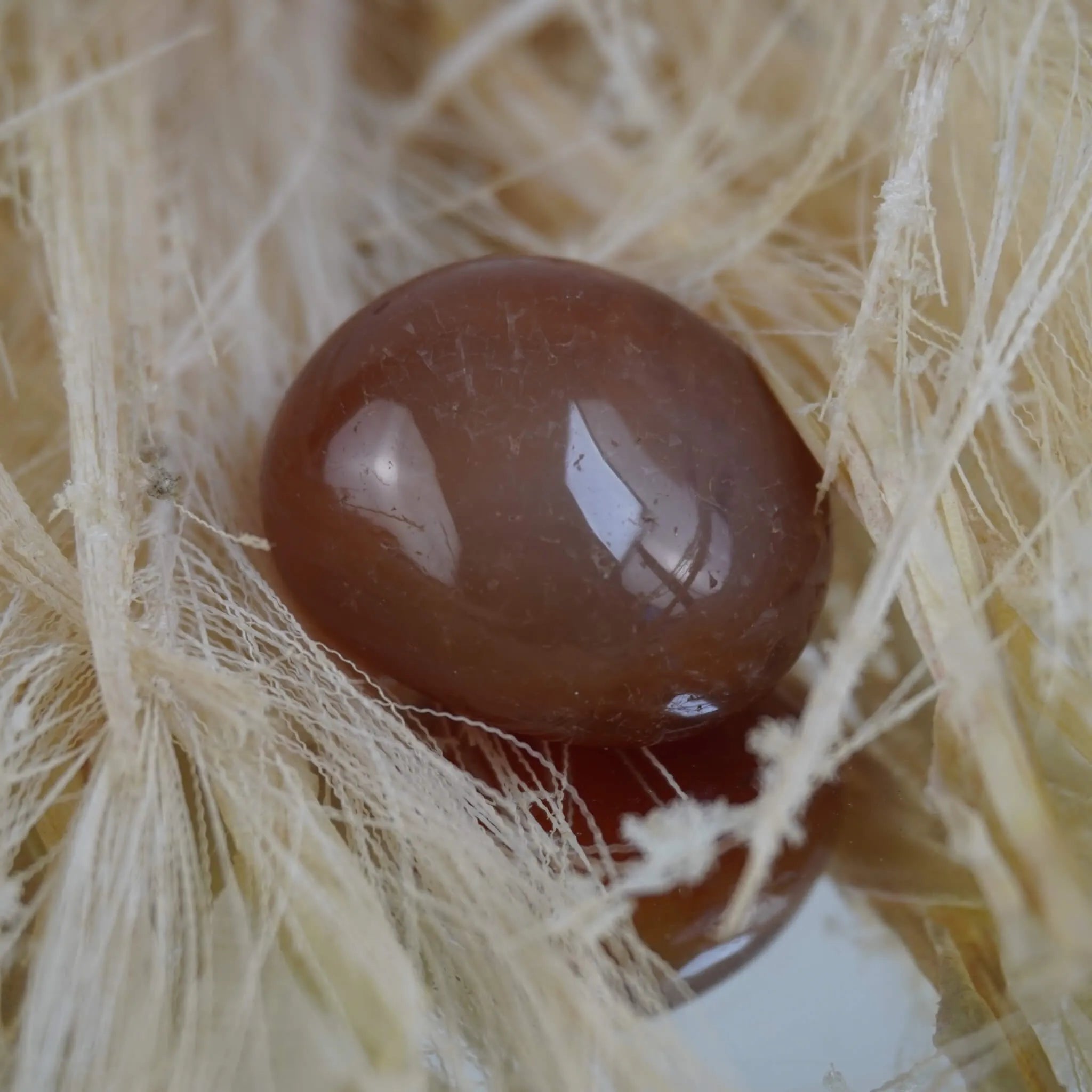 Karneol Trommelstein in warmem Orange auf hellen Naturfasern