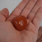 Glatter Karneol Trommelstein in kräftigem Orange in einer geöffneten Hand