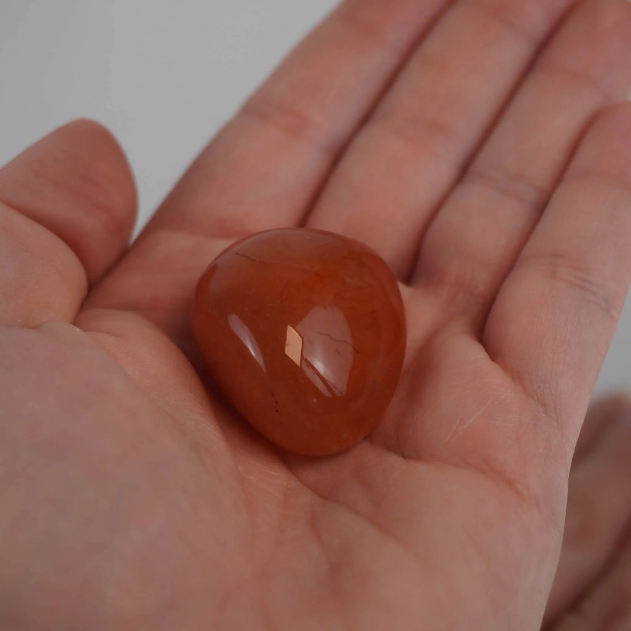 Glatter Karneol Trommelstein in kräftigem Orange in einer geöffneten Hand
