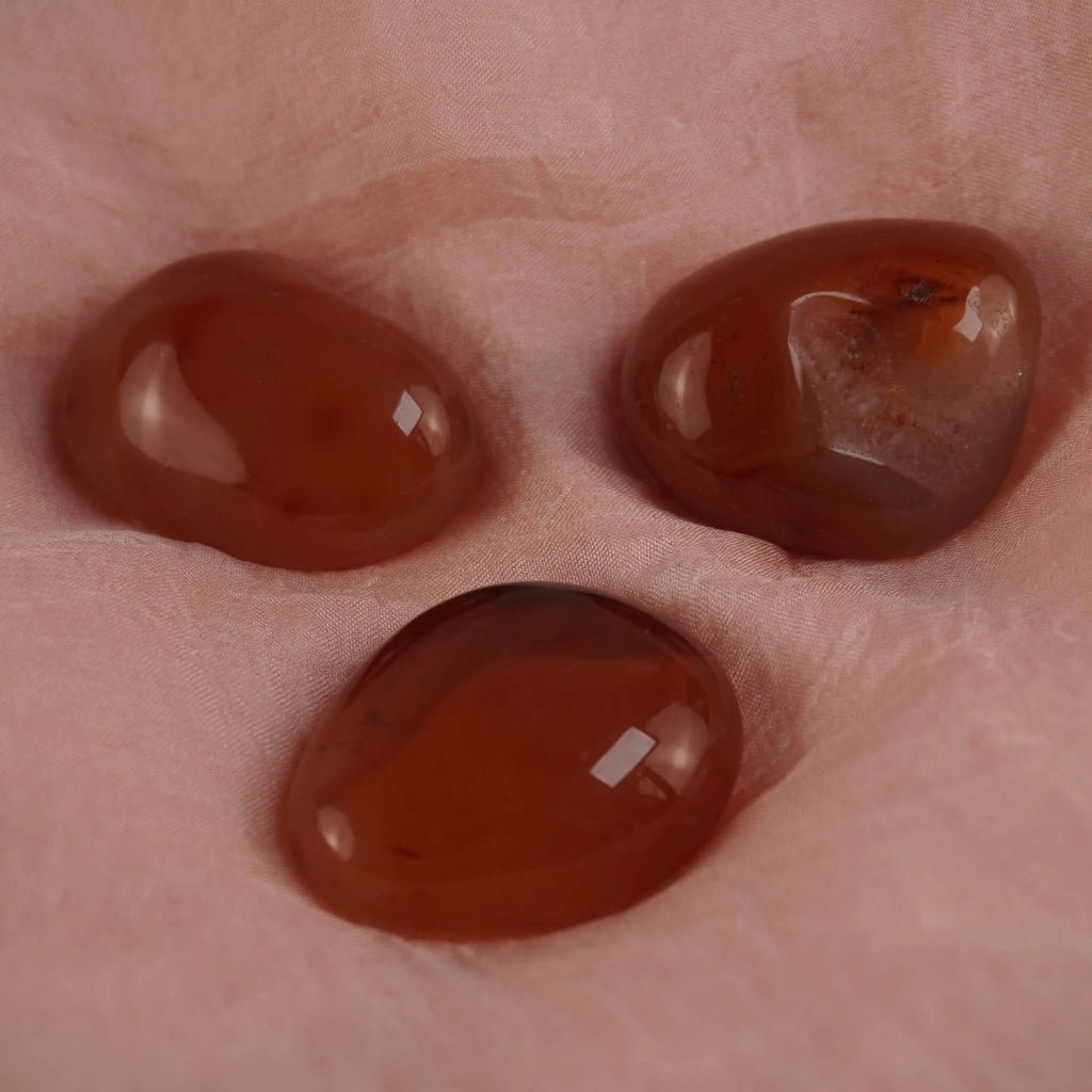 Drei orangefarbene Karneol Trommelsteine auf weichem rosafarbenem Stoff