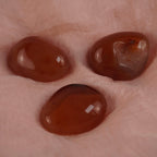 Drei orangefarbene Karneol Trommelsteine auf weichem rosafarbenem Stoff