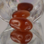 Mehrere Karneol Trommelsteine in transparenter Glasschale mit Spiegelung arrangiert