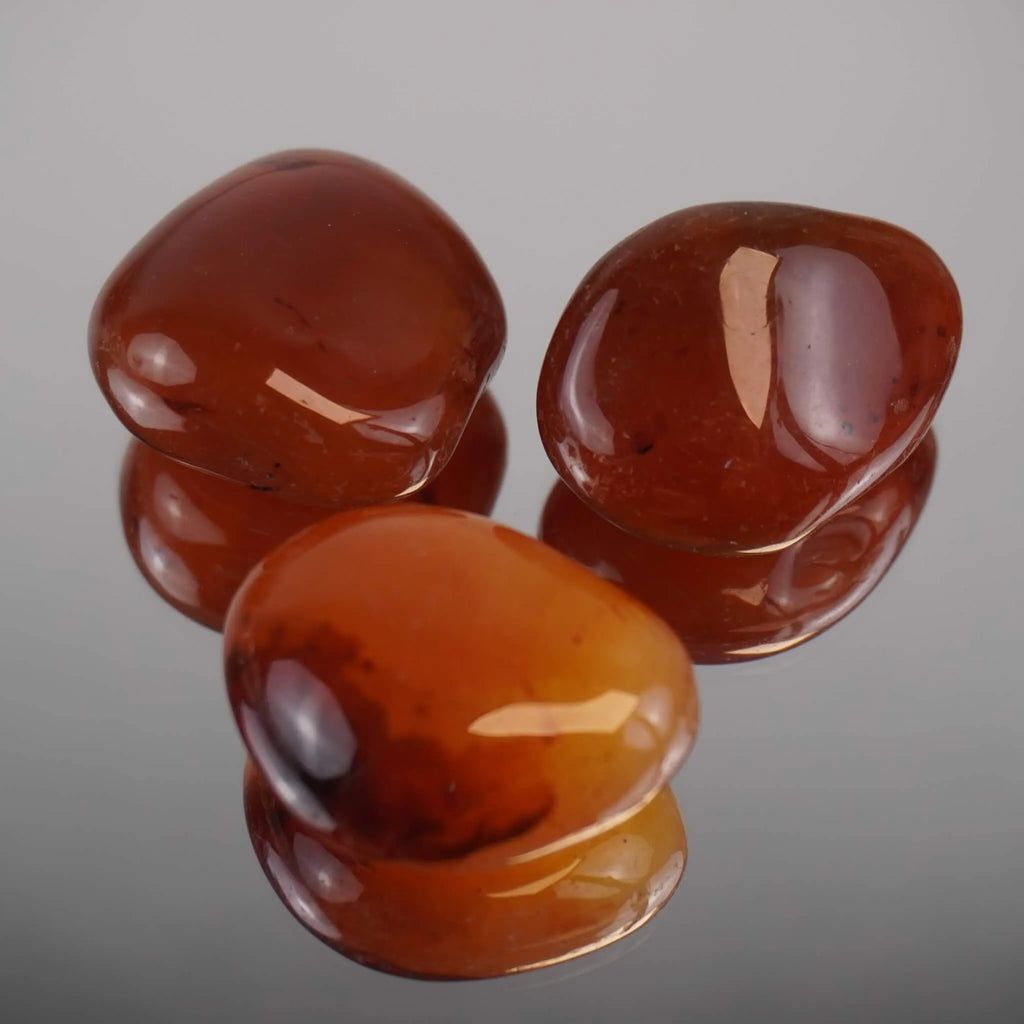 Drei polierte Karneol Trommelsteine mit Spiegelung auf glänzender Unterlage