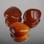 Drei polierte Karneol Trommelsteine mit Spiegelung auf glänzender Unterlage