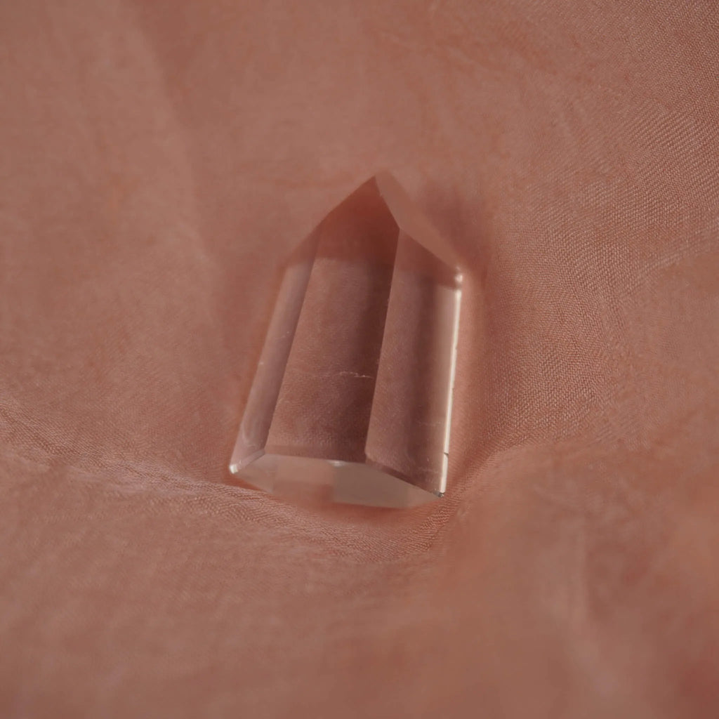 Polierte klare Bergkristall Spitze liegend auf zart rosafarbenem Stoff