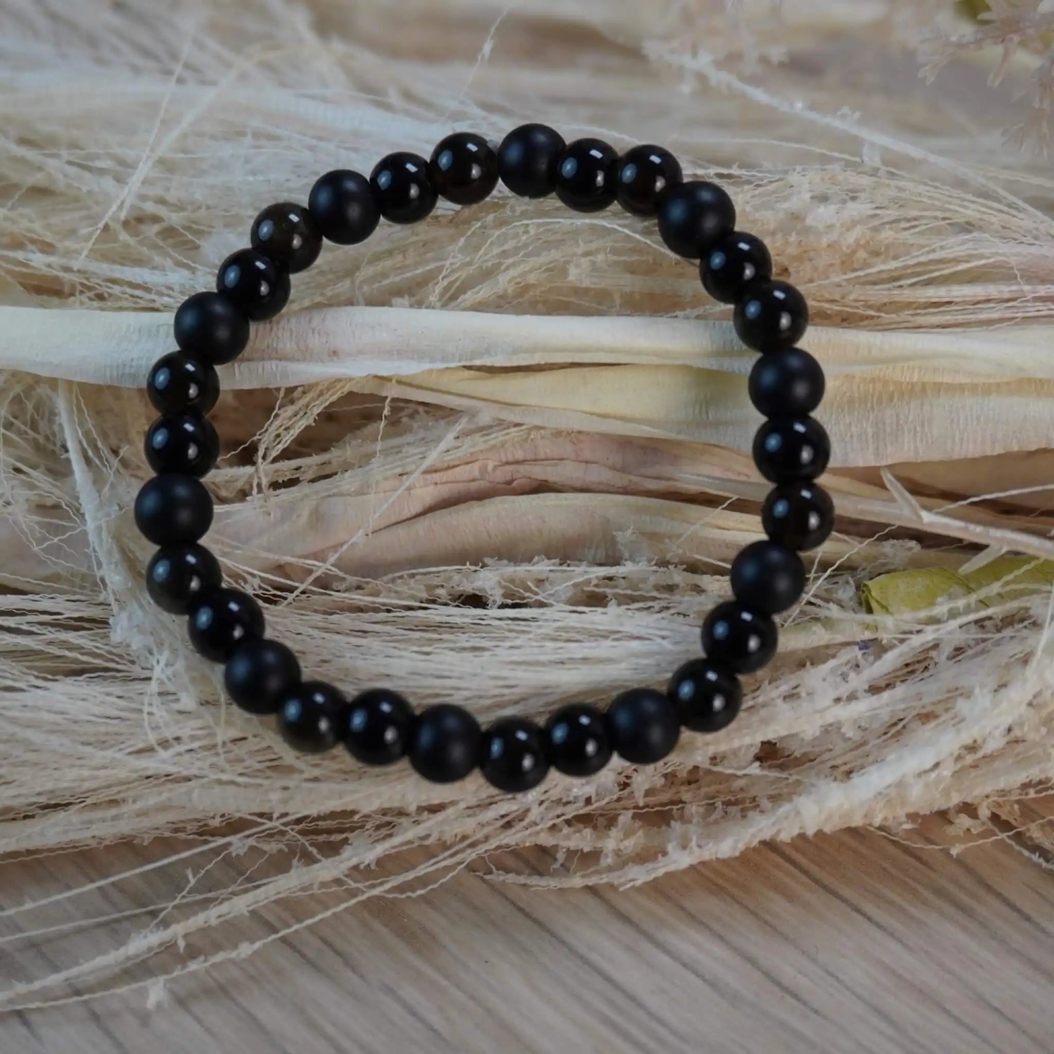 Kugelarmband aus Onyx, Obsidian und Turmalin auf hellem Trockengras dekoriert