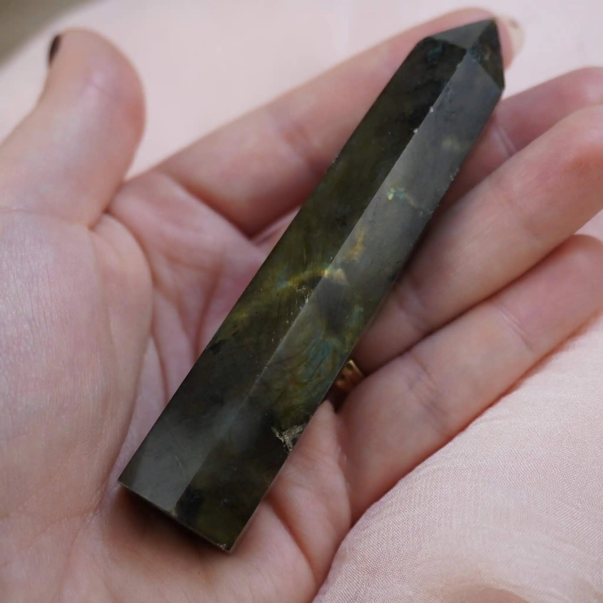 Labradorit Obelisk Kristall in einer Hand gehalten, schimmernde Facetten sichtbar