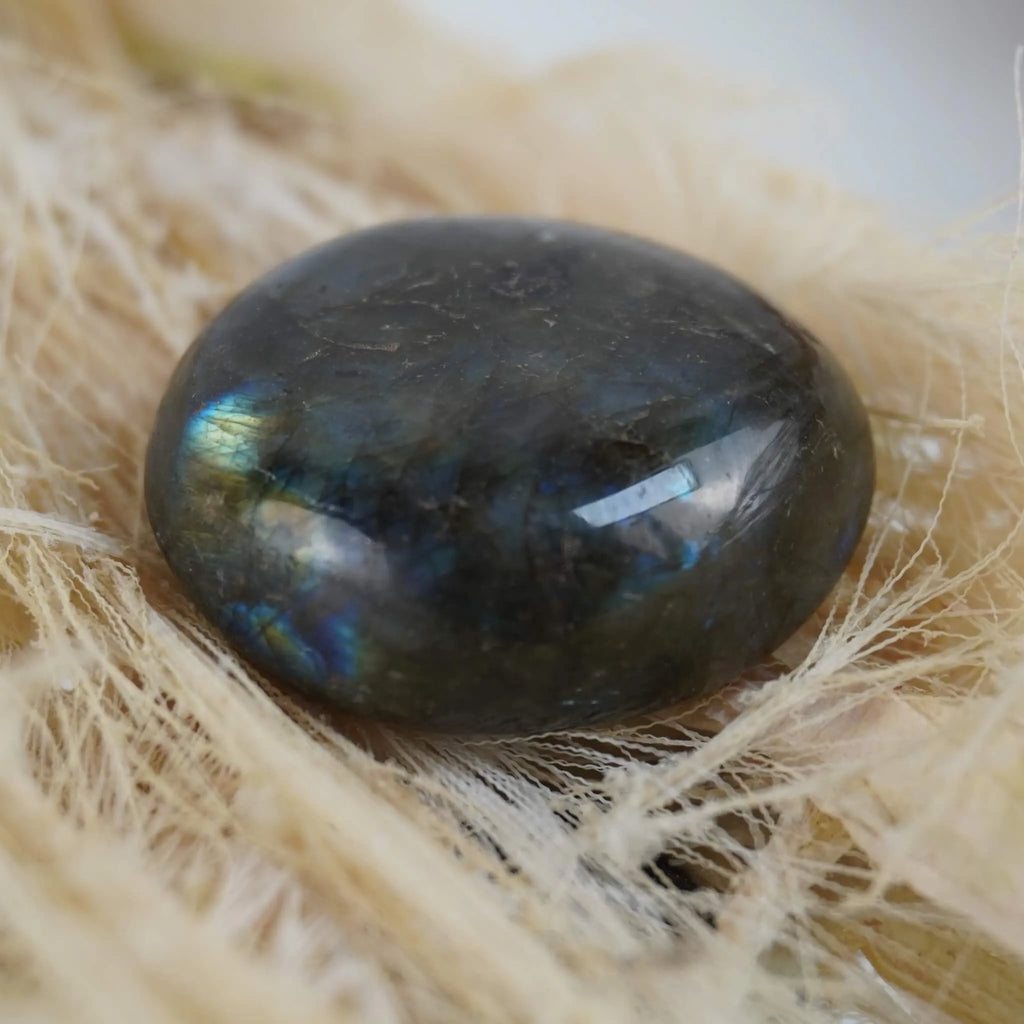 Labradorit Trommelstein mit blaugrüner Irisierung auf hellen Naturfasern