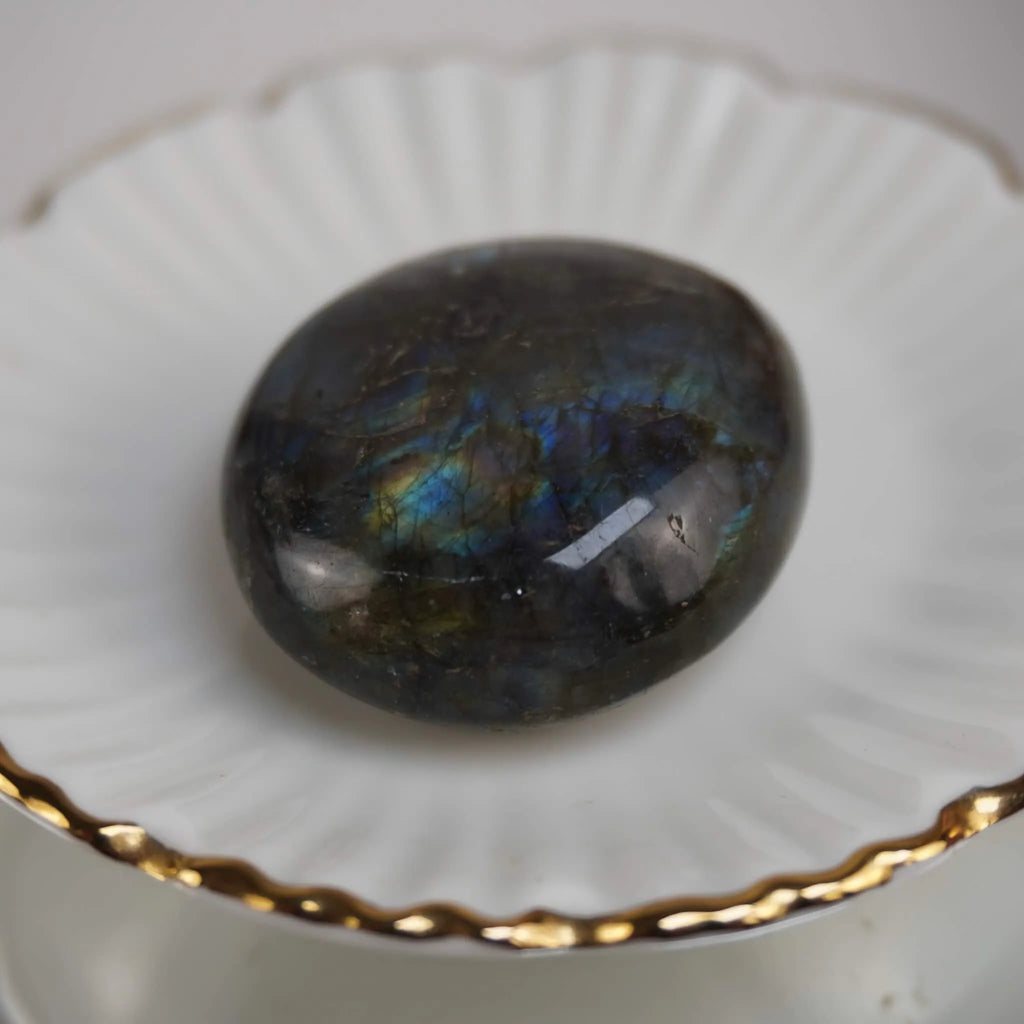 Labradorit Trommelstein mit blauem Farbspiel auf weißer Schale mit Goldrand