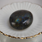 Labradorit Trommelstein mit blauem Farbspiel auf weißer Schale mit Goldrand