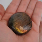 Flacher Labradorit Trommelstein mit warmem goldbraunem Schimmer in einer geöffneten Hand