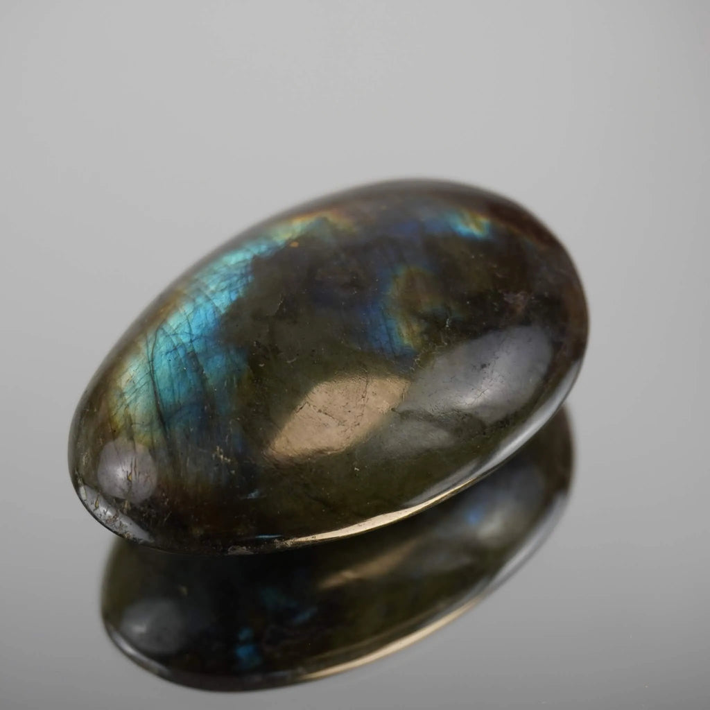 Polierter Labradorit Trommelstein mit blaugrünem Schimmer und Spiegelung auf glänzender Fläche
