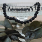 Lavastein Kugelarmband an Glas-Schale mit dunklen Eukalyptusblättern arrangiert