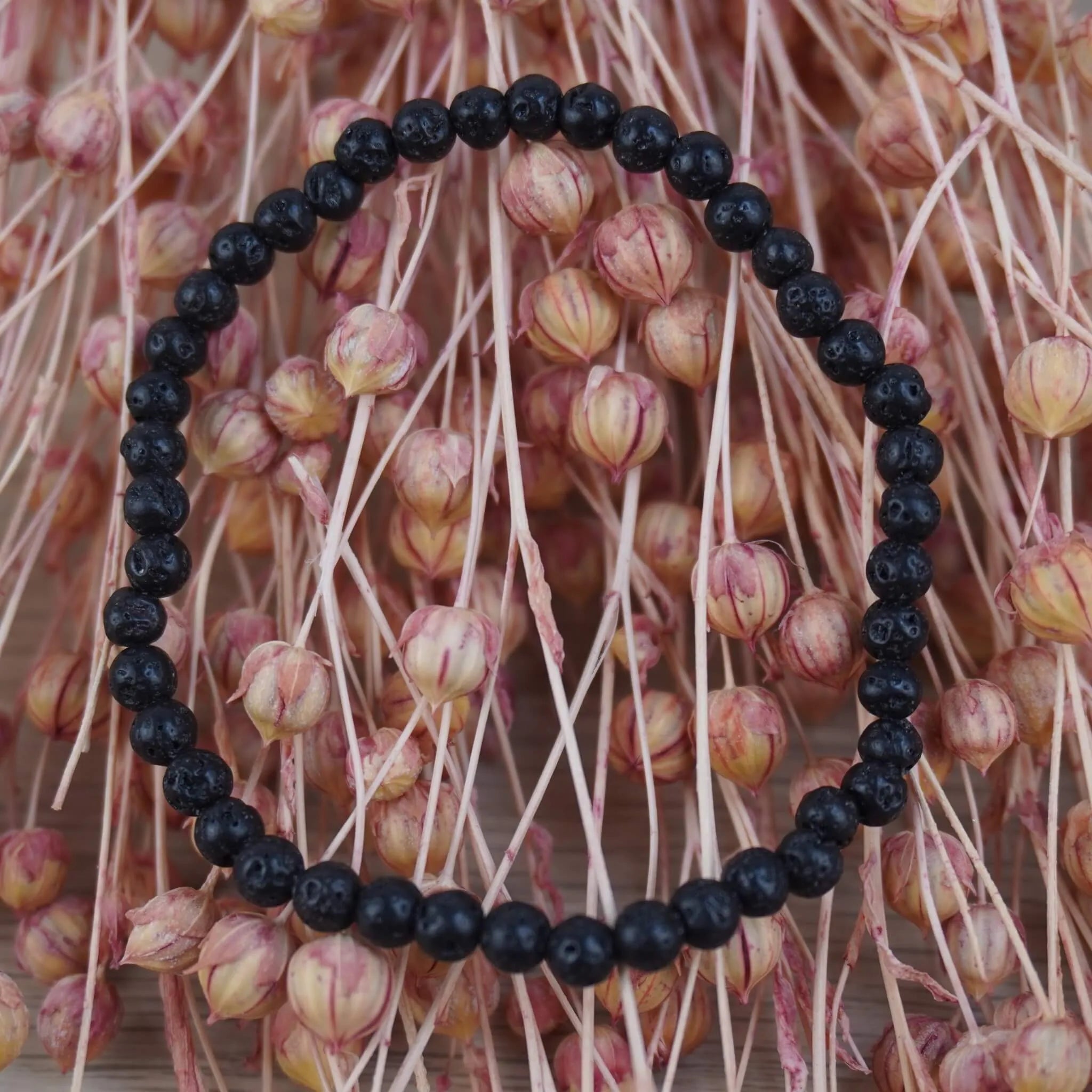 Lavastein Kugelarmband vor rosafarbenen Trockenblumen natürlich dekoriert