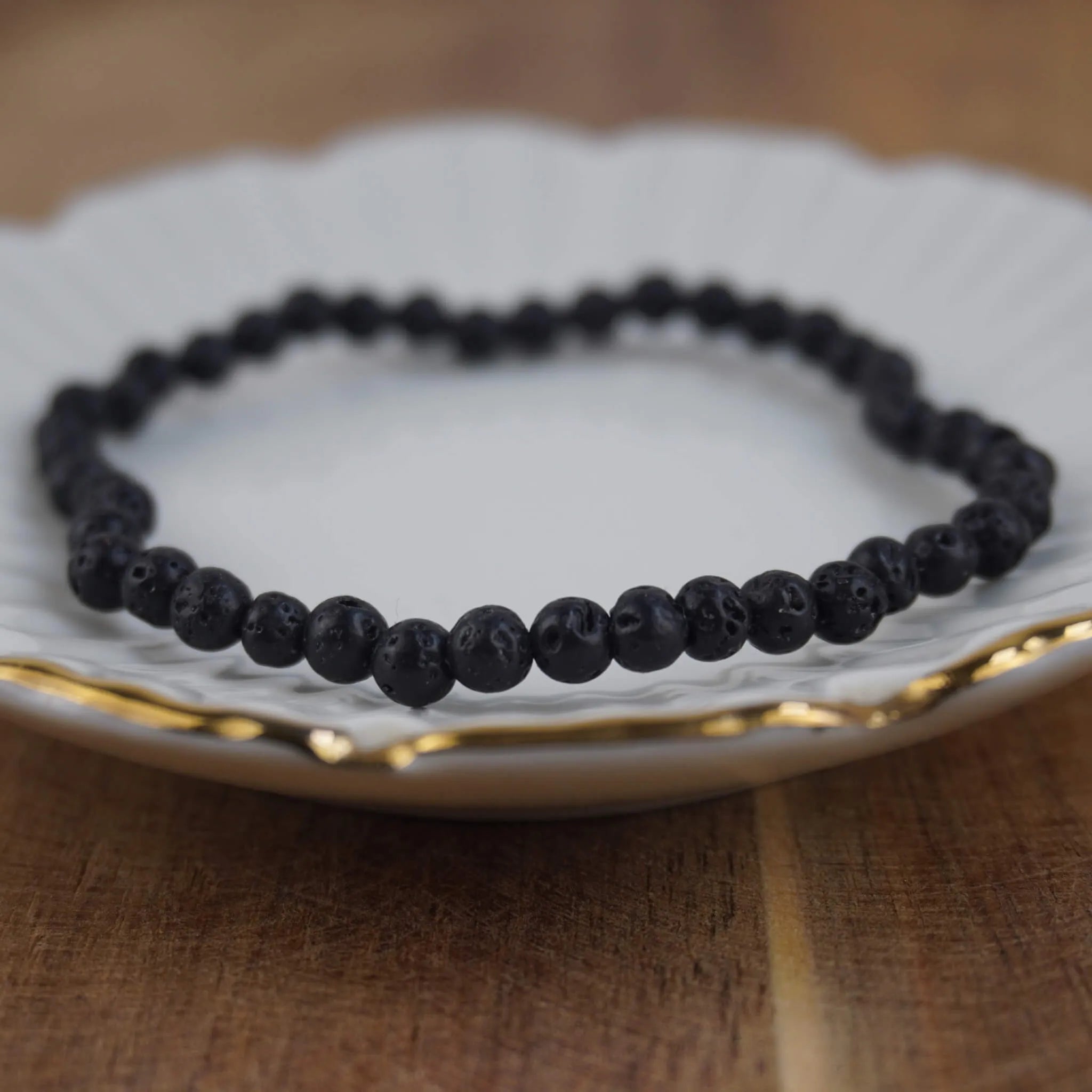 Lavastein Kugelarmband auf weißem Teller mit elegantem Goldrand