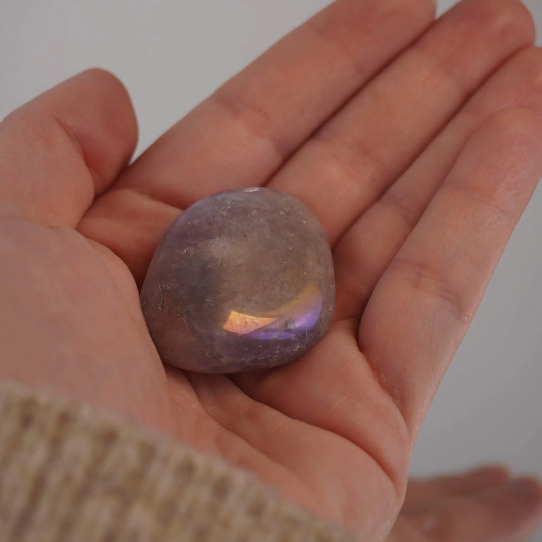 Lila Angel Aura Trommelstein mit irisierendem Schimmer in einer Hand liegend