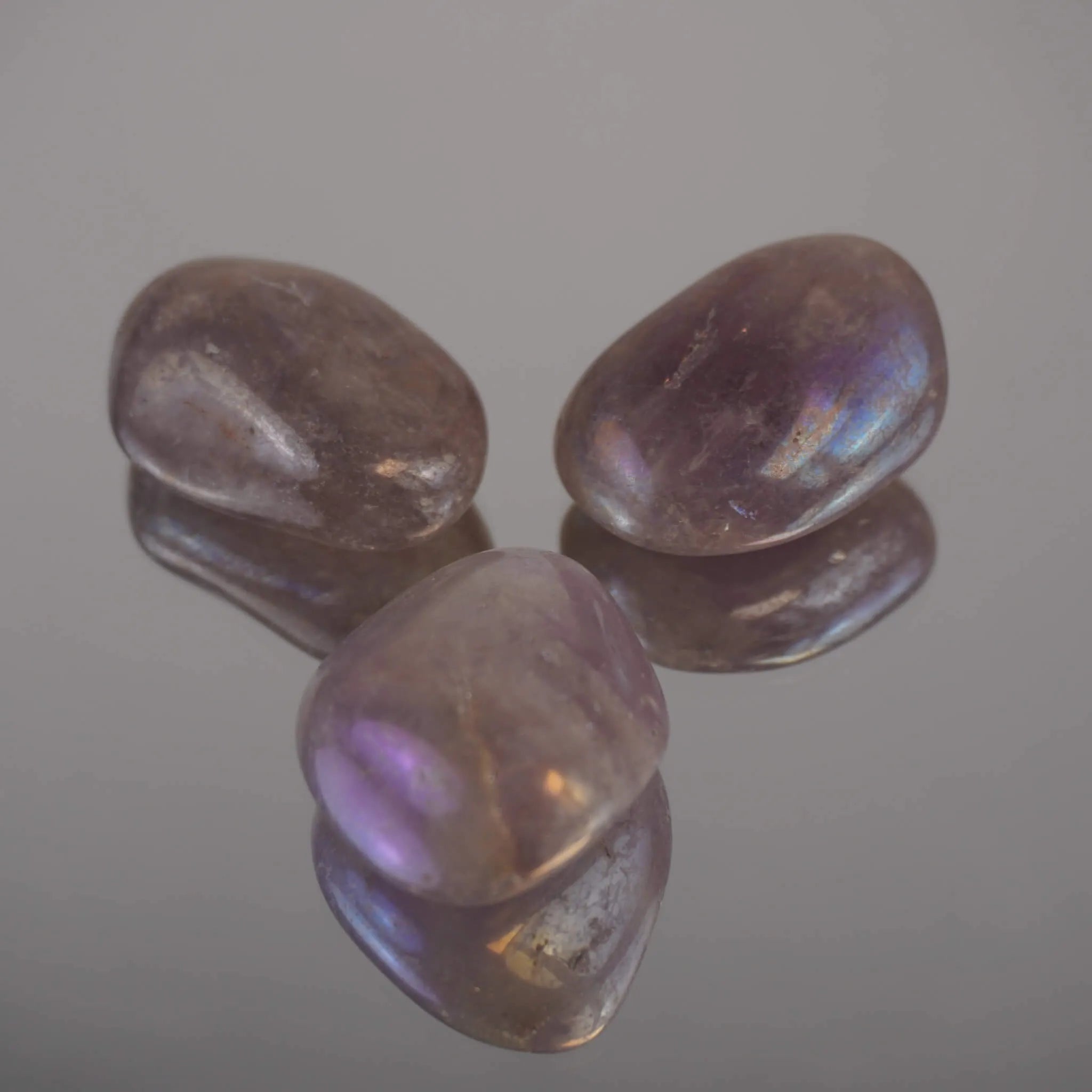 Drei Lila Angel Aura Trommelsteine mit schimmerndem Regenbogenglanz auf Spiegel arrangiert