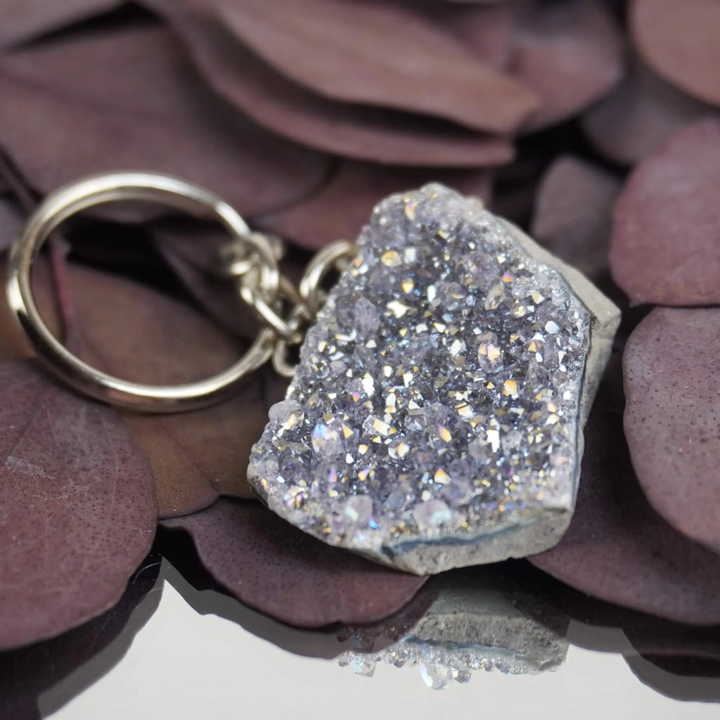 Schimmernder Lila Aqua Aura Druse Schlüsselanhänger auf violetten Blättern mit Spiegelung