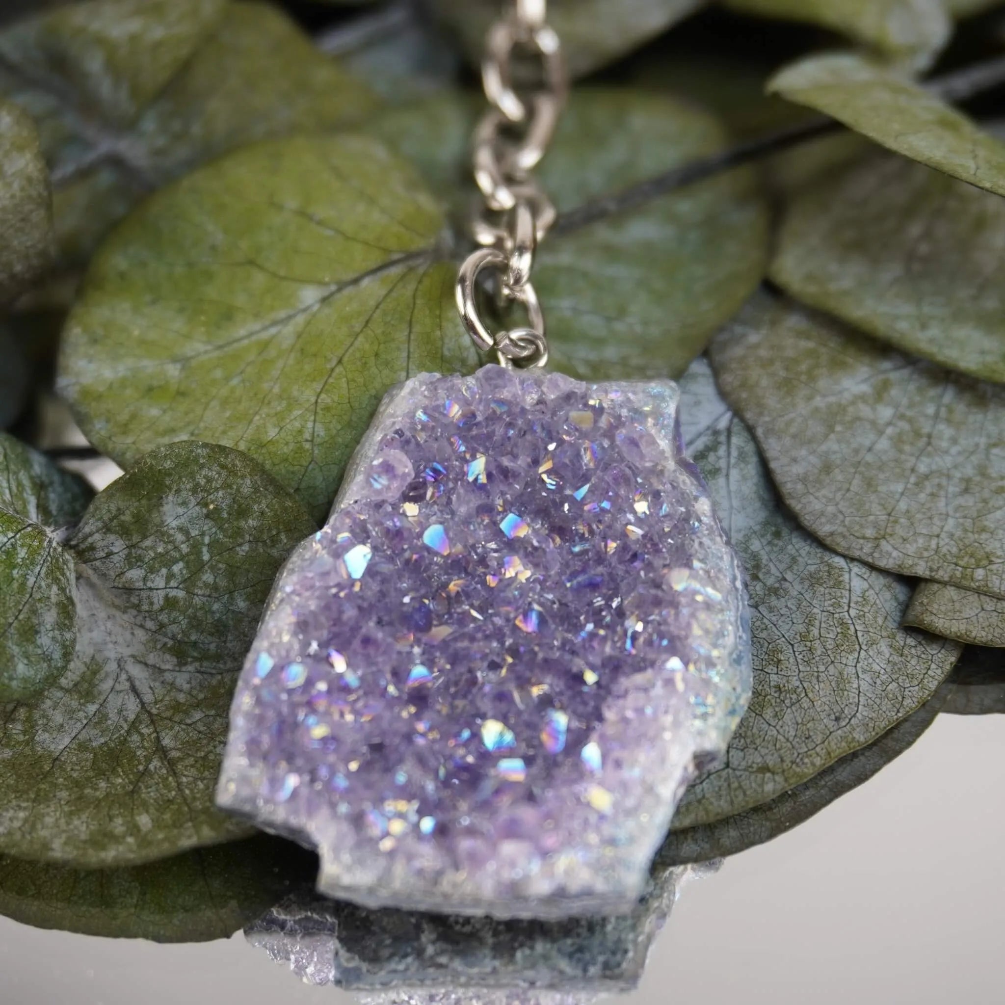 Lila Aqua Aura Druse Schlüsselanhänger dekoriert auf grünen Eukalyptusblättern