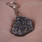 Funkelnder Lila Aqua Aura Druse Schlüsselanhänger präsentiert auf rosafarbenem Stoff