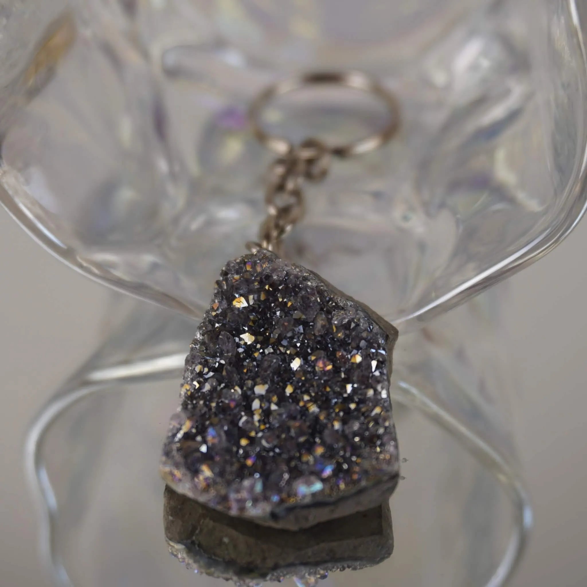 Lila Aqua Aura Druse Schlüsselanhänger mit funkelnder Kristallfläche vor transparenter Glasdeko