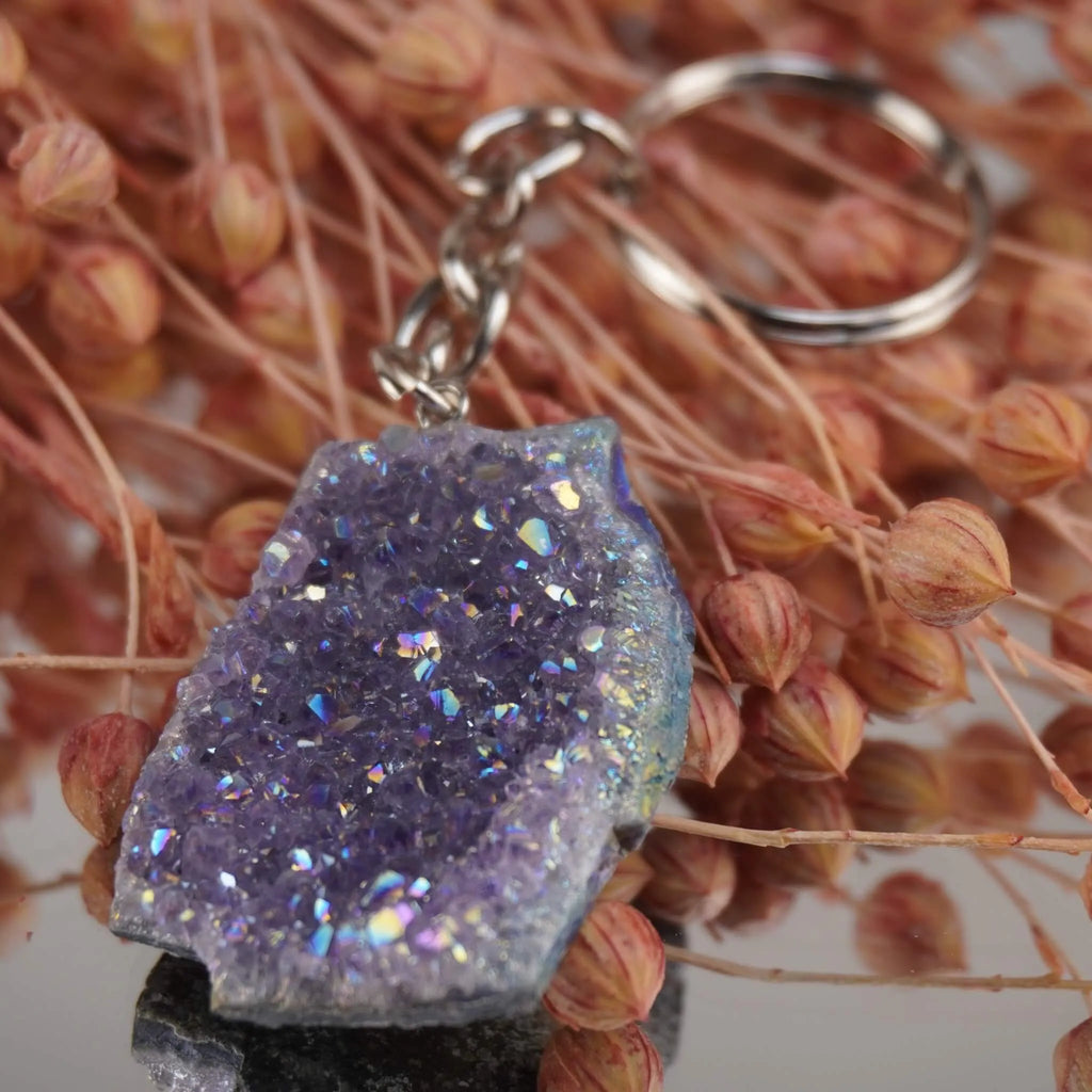 Lila Aqua Aura Druse Schlüsselanhänger mit funkelnder Oberfläche vor rosa Trockenblumen arrangiert