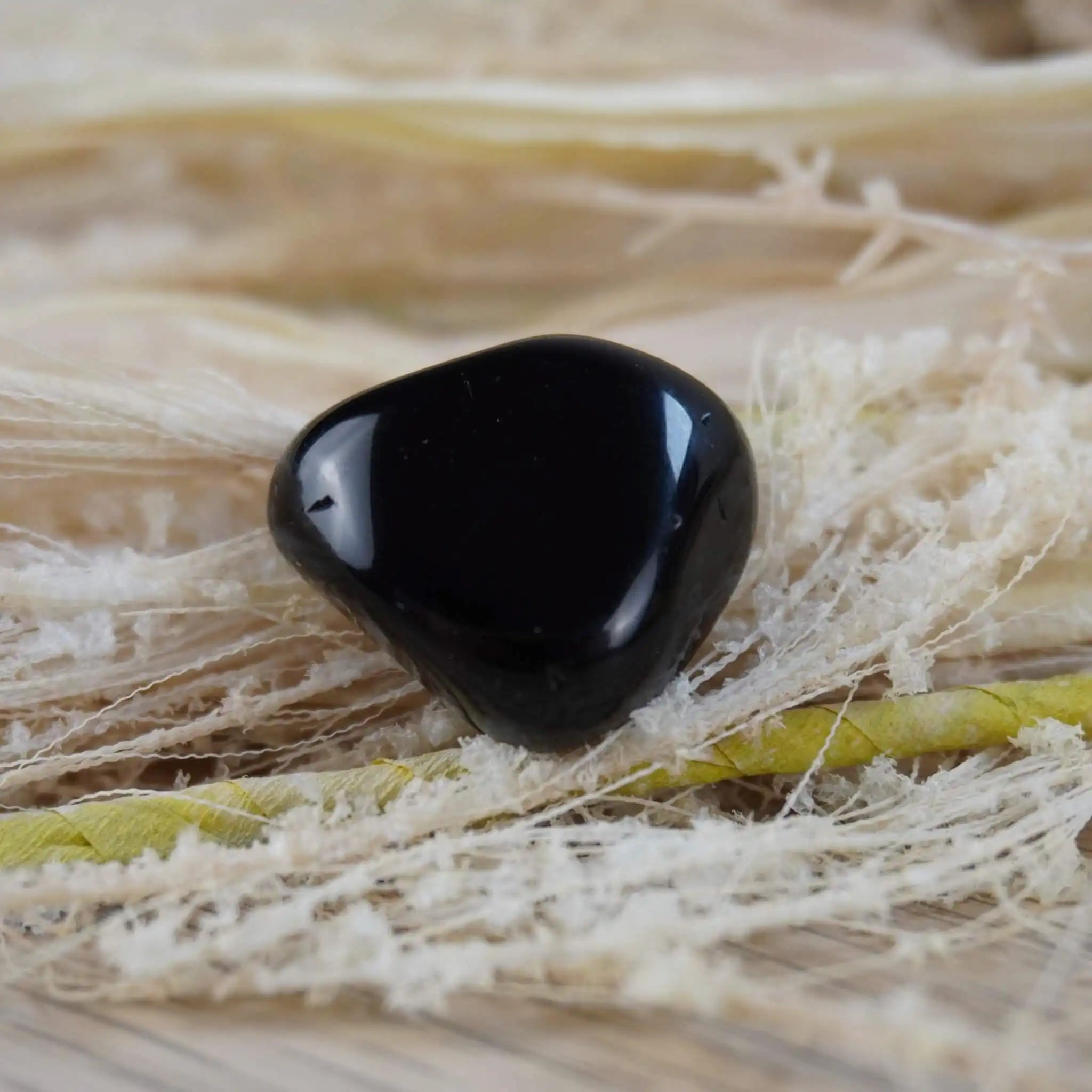 Obsidian Trommelstein auf hellem Naturfaser-Hintergrund